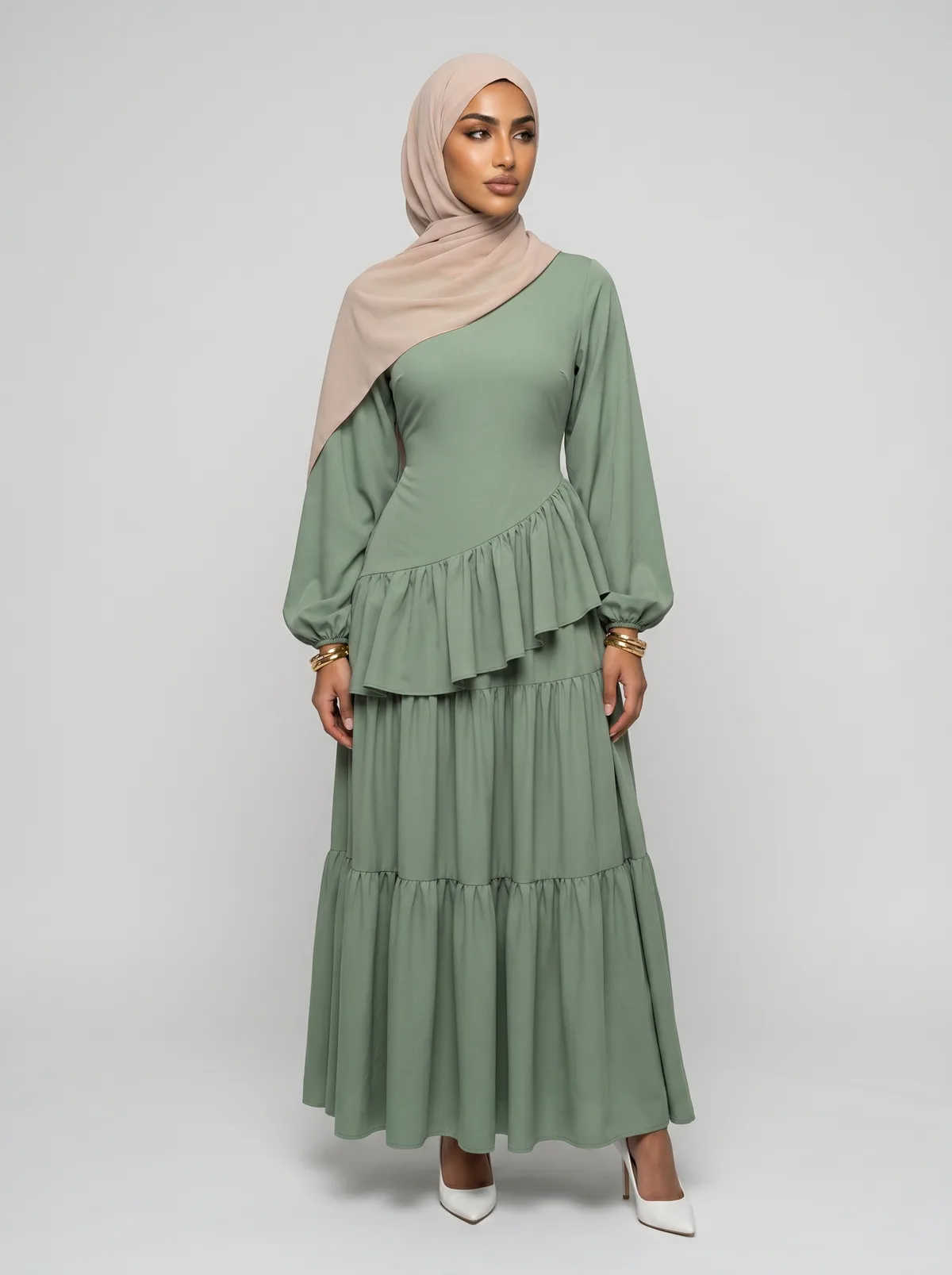 Hijabi fashion model wearing a sage green draped dress in a full-length studio view